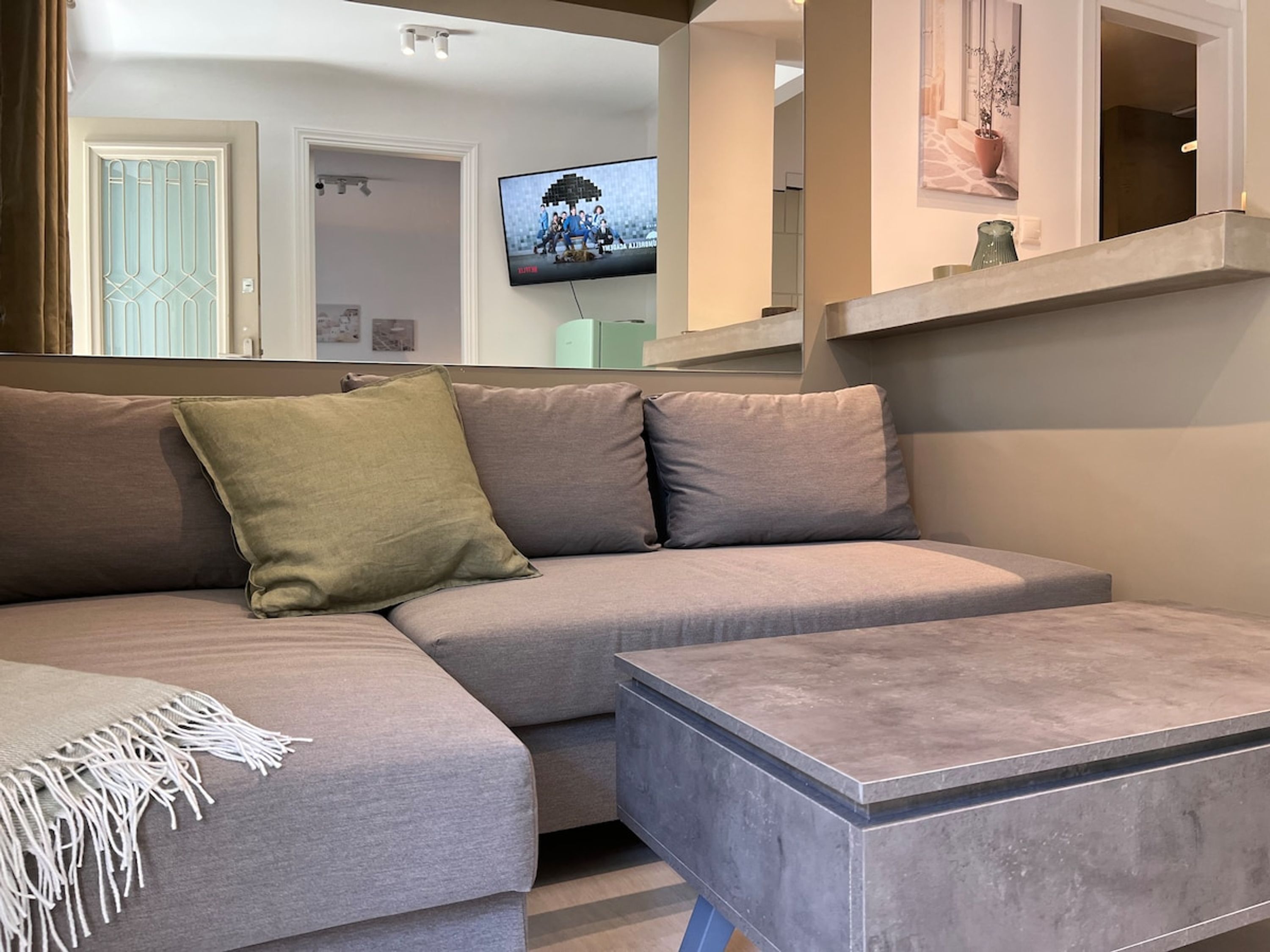 A modern living room with a grey sectional sofa, a small coffee table, and a flat-screen TV mounted on the wall.