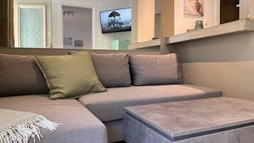 A modern living room with a grey sectional sofa, a small coffee table, and a flat-screen TV mounted on the wall.