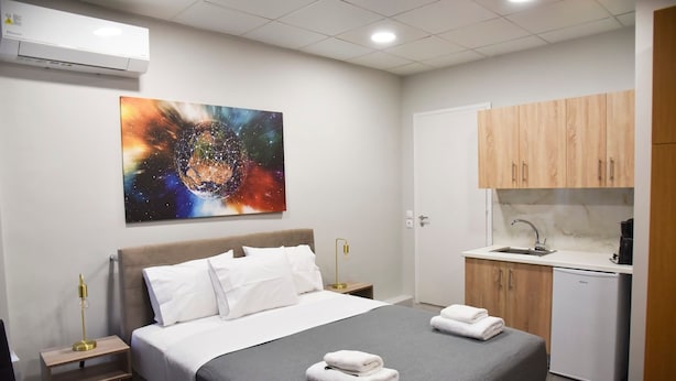 Een hotelkamer met een bed, een schilderij, een bureau, een stoel, een wastafel en een klein keukenhoekje.