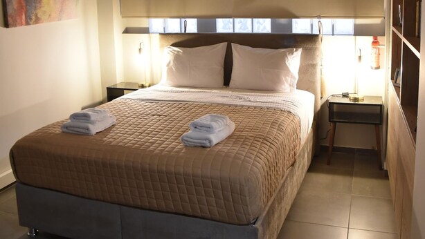 A hotel room with a large bed, a bedside table, a nightstand, and a bookshelf. - Athens Ianos B by Super Host Hub (Μενεμένη)