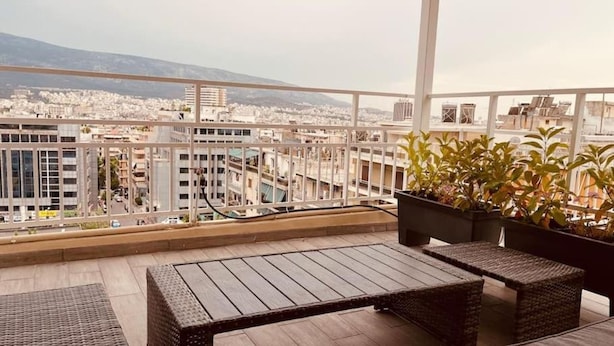 Ein Balkon mit Korbmöbeln, Topfpflanzen und Blick auf die Stadt.