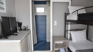 Ein kompaktes Hotelzimmer mit Etagenbett, kleinem Schreibtisch und Fernseher sowie einer Dusche.