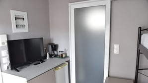 Ein kompaktes Zimmer mit Flachbildfernseher, einer Kaffeemaschine und einem kleinen Kühlschrank.