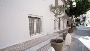 Una vorera amb plantes en testos i un edifici blanc amb reixes.