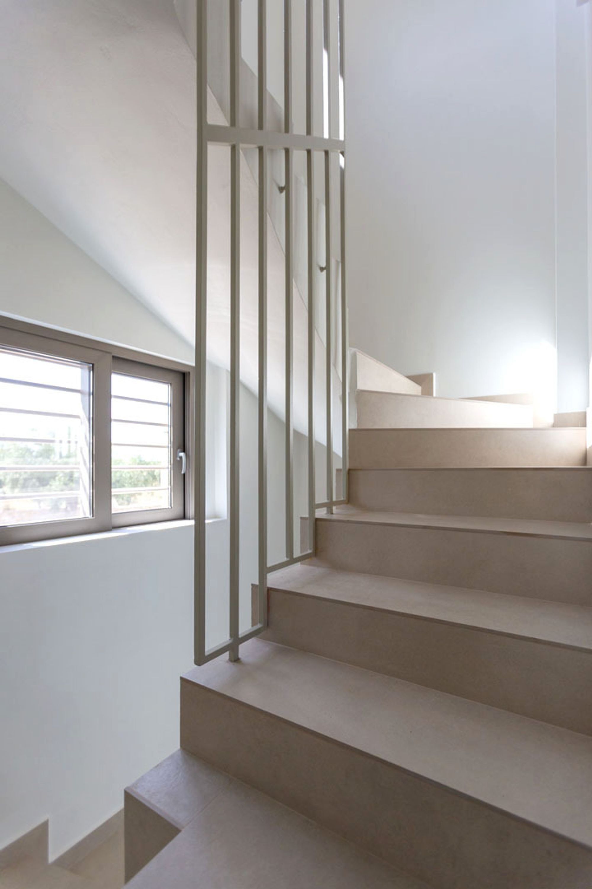 Un escalier avec une rampe en métal, menant à un palier doté d’une fenêtre.