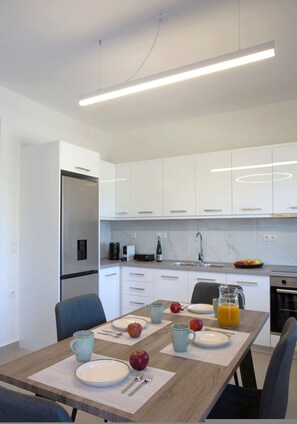 Una cocina moderna con armarios blancos, un refrigerador empotrado y un comedor con una mesa de madera dispuesta para el desayuno.