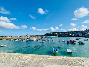 A harbor with numerous boats docked, a stone pier, and a distant view of a town with buildings and a hill. - St Ives Cottage, 2 minutes walk to beach & town, garden, sleeps 6, pets welcome (St Ives)
