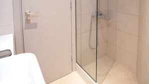 Une douche fermée par des parois en verre, dotée d’un pommeau de douche à main et d’un robinet mural.