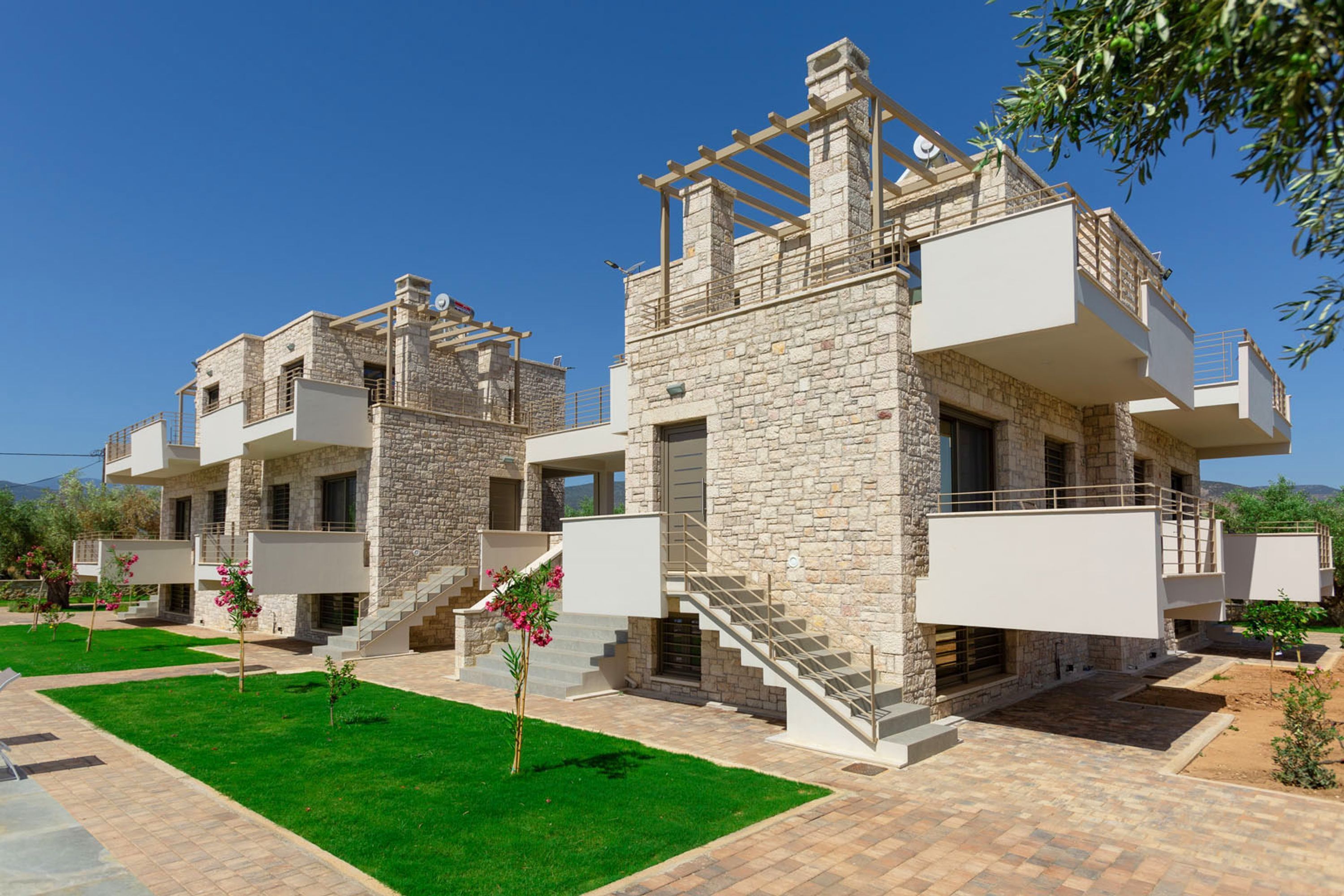 Un bâtiment moderne à deux étages, doté d’une façade en pierre, de balcons et d’une pelouse bien entretenue.