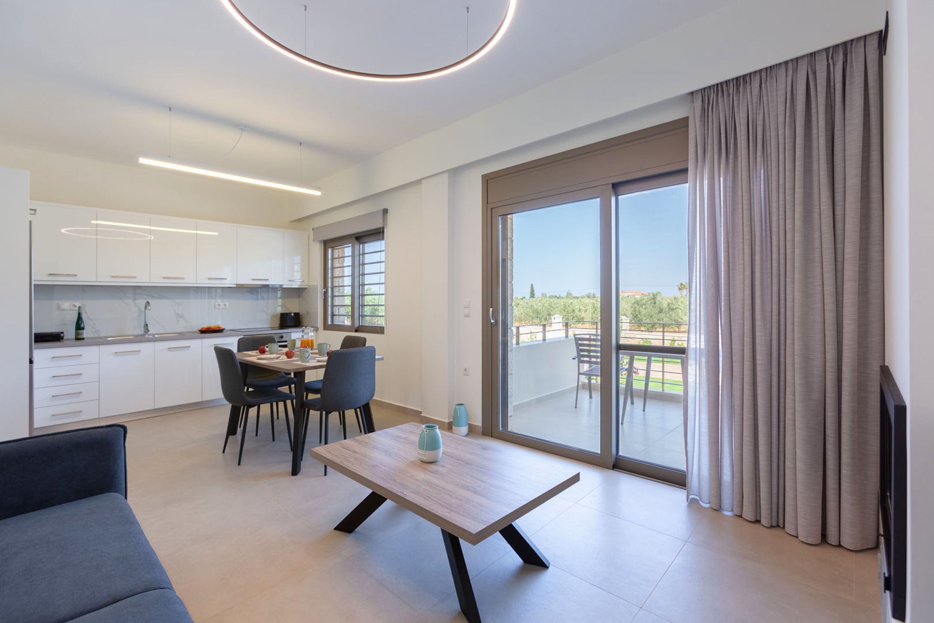 Une cuisine moderne avec des meubles blancs, un coin repas comprenant une table et des chaises, et une grande porte-fenêtre coulissante donnant sur une terrasse ext érieure.