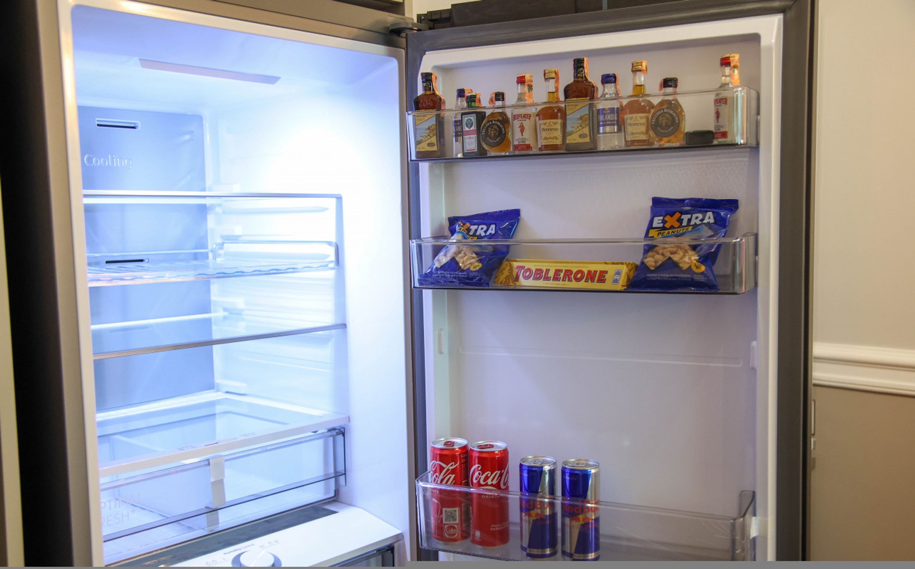 Un réfrigérateur doté de plusieurs étagères contenant diverses boissons, des en-cas et quelques canettes de soda.