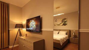 A hotel room with a bed, a desk, a lamp, a TV mounted on the wall, and a painting. - Grandstay Apartments 001 (Durrës)