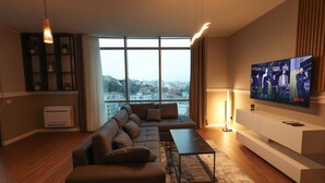 A modern living room with a large window, a sectional sofa, a flat-screen TV, and a minimalist design. - Grandstay Apartments 001 (Durrës)