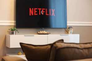 A living room with a TV displaying the Netflix logo, a white cabinet, a small plant, and a model house. - Grandstay Apartments 002 (Durrës)