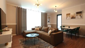 Un salon moderne avec un canapé d’angle, une table basse et un coin repas doté de chaises vertes.