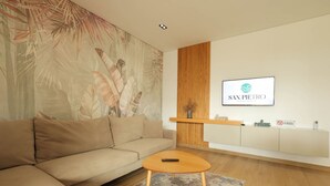 Una sala de estar moderna con un sofá color beige, una mesa de centro redonda, un televisor montado en la pared y un cartel que indica 'NO FUMAR'.