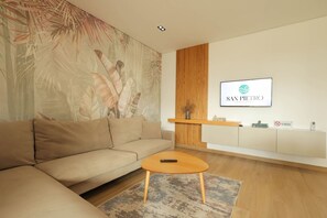 A modern living room with a beige sofa, a round coffee table, a wall-mounted TV, and a 'NO SMOKING' sign. - Sanpietro Vacation Apartment 001 (Plazhi San Pietro)