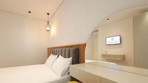 Una habitación de hotel moderna con una cama, un escritorio, una silla, un televisor y un espejo.