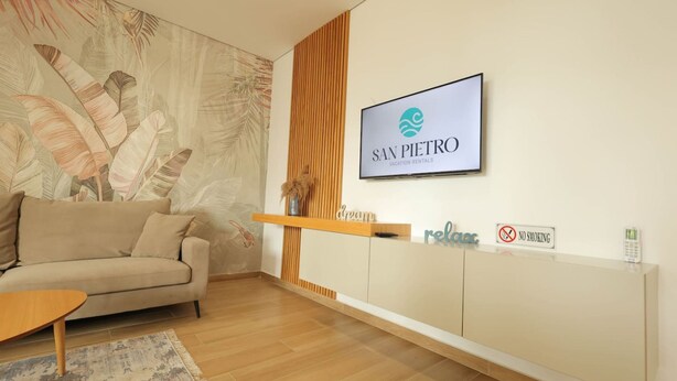 Un área de recepción con un sofá, un mueble de madera, un cartel de 'San Pietro Vacation Rentals', un letrero de 'No Fumar' y una pared decorativa con motivos de hojas.