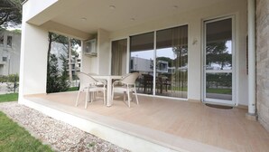 Un patio exterior moderno con mesa y sillas, grandes puertas correderas de vidrio y un equipo de aire acondicionado pequeño.