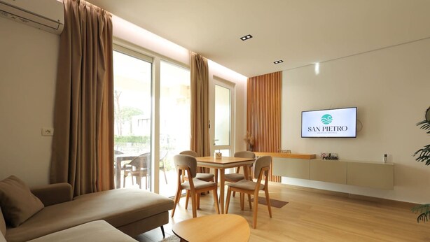 Un salon moderne avec un canapé, une table à manger et des chaises. Un téléviseur à écran plat est fixé au mur.