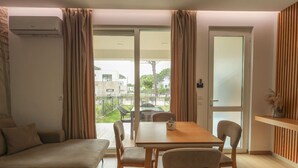 Un salon moderne avec un canapé, une table à manger et des chaises. Une porte-fenêtre coulissante donne accès à un balcon offrant une vue sur l’extérieur.
