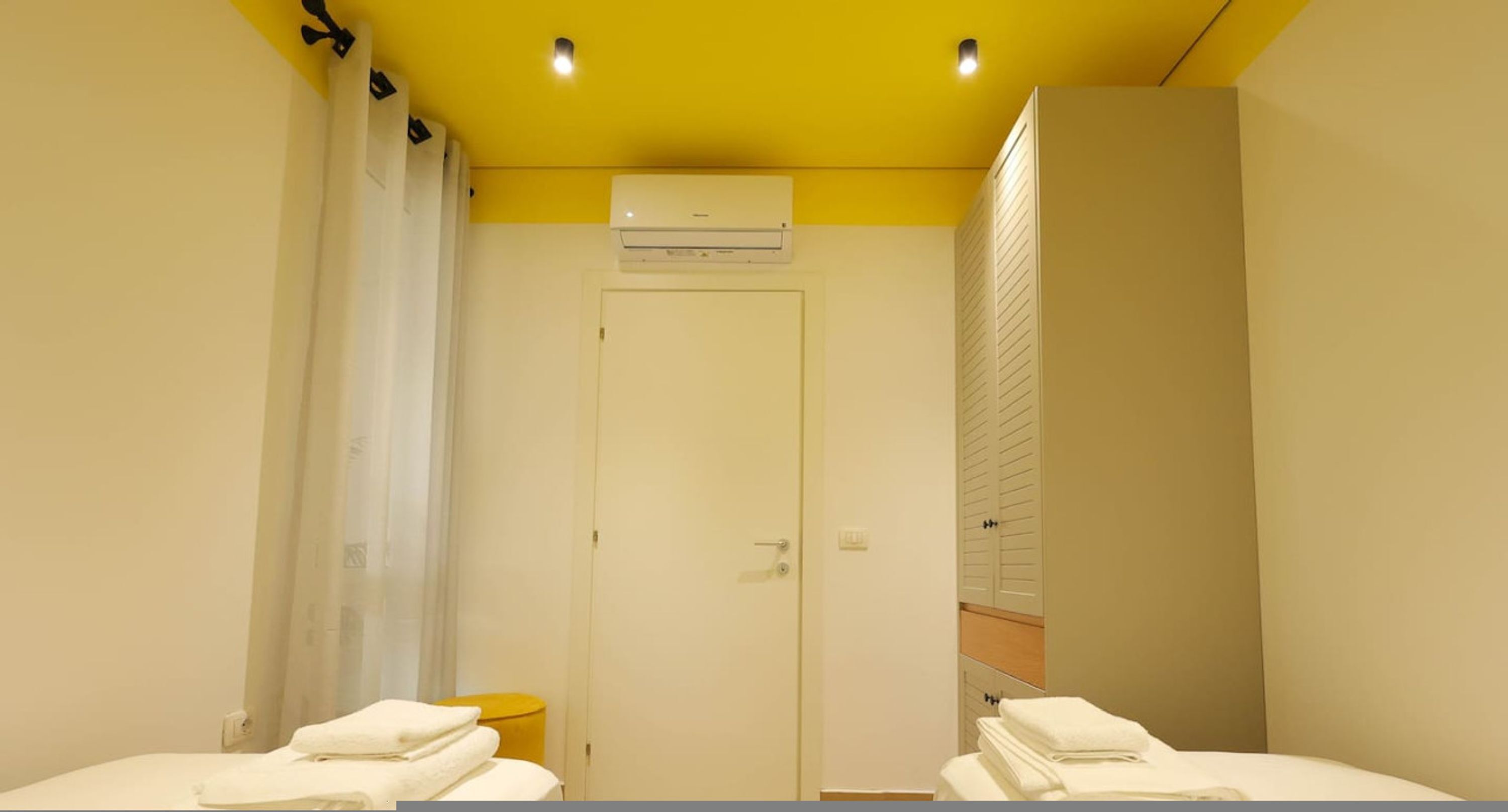 A hotel room with a yellow ceiling, a white door, and two beds with white towels.