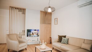 Un soggiorno moderno con un divano color beige, una poltrona abbinata, un tavolino e una TV su un mobile.