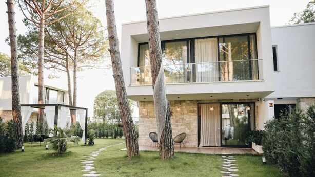 Una moderna casa a due piani con facciata in pietra, una zona relax all'aperto coperta e un vialetto in pietra che conduce all'ingresso.