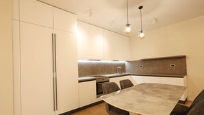 A modern kitchen with white cabinets, a built-in oven, a dining table with chairs, and pendant lighting. - Grandstay Portside in Durrës (Durrës)