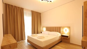 Een moderne hotelkamer met een groot bed, een houten hoofdbord, nachtkastjes en een groot raam met gordijnen.
