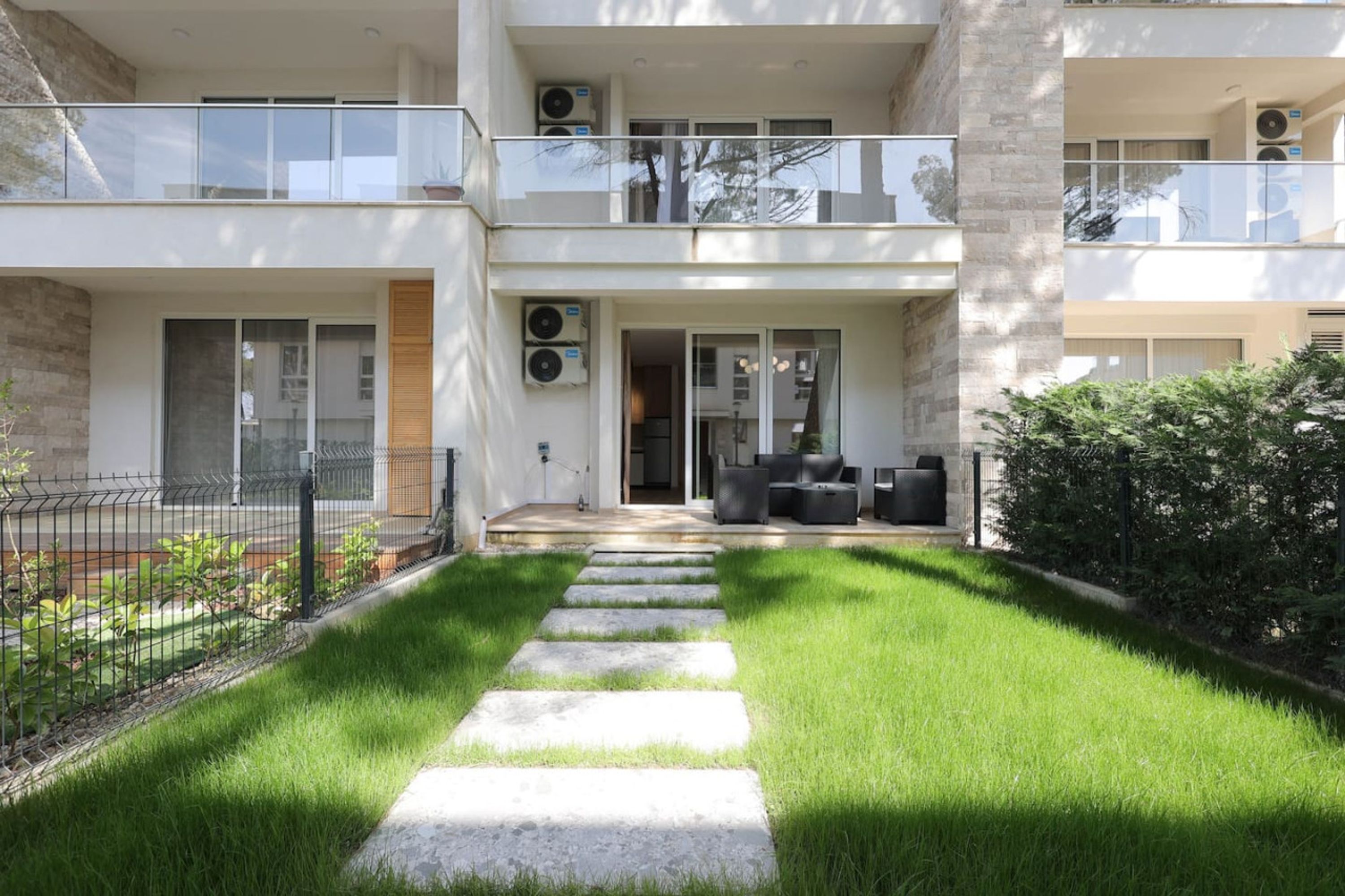 A modern two-story building with a covered outdoor seating area, a well-maintained lawn, and a stone pathway leading to the entrance.