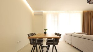 Ein modernes Wohnzimmer mit einem Holzesstisch, sechs Stühlen, einem beige farbenen Sofa und einem Blumentopf.