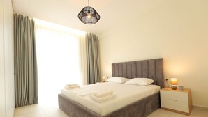 Ein ordentlich bezogenes Bett mit Kissen und gefalteten Handtüchern, ein Nachttisch mit Lampe sowie eine Hängelampe.