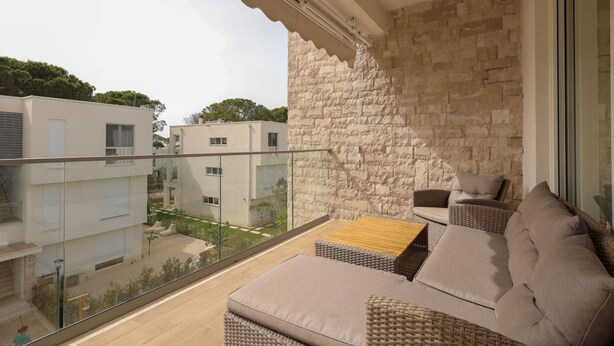 Ein Balkon mit Korbmöbeln, einer Steinwand und Blick auf benachbarte Gebäude.