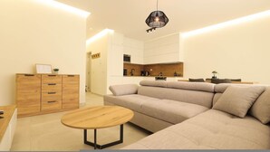 Ein modernes Wohnzimmer mit einer Couch, einem Holztisch und einer Küchenzeile im Hintergrund.