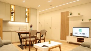 Una sala moderna con comedor, un televisor que muestra 'SAN PIETRO Vacation Rentals' y una cocina con estantes empotrados.