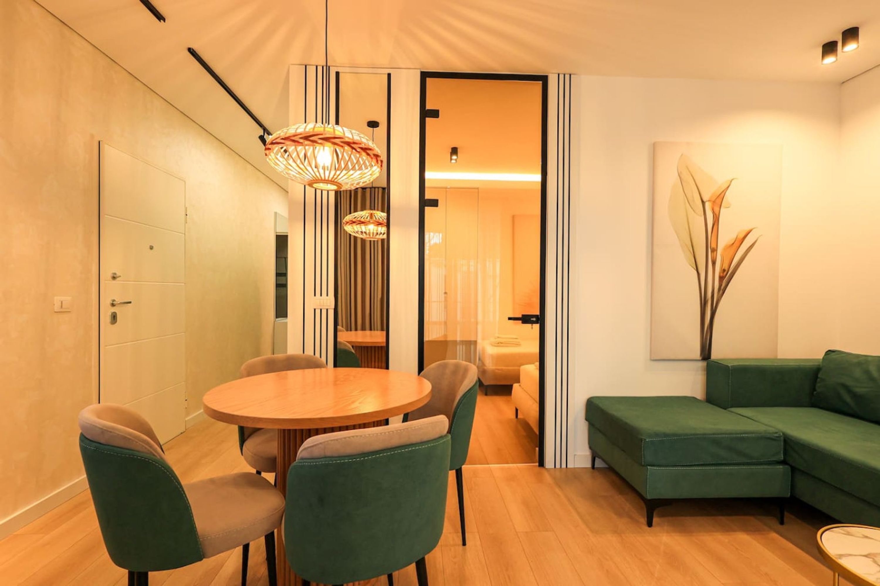 Een moderne woonkamer met een groene bank, een ronde houten eettafel met stoelen, en een hanglamp.