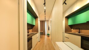 Una cocina moderna y estrecha con suelo de madera, armarios verdes y una isla central.