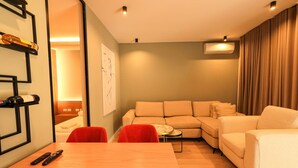 A modern living room with a sectional sofa, a wooden dining table, and a small side table. - SanPietro Vacation Apartment 026 (Plazhi San Pietro)