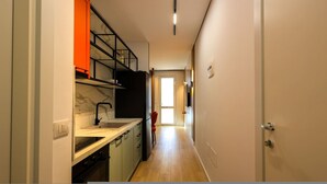 A narrow hallway leading to a kitchen with a sink, stove, and shelves. - SanPietro Vacation Apartment 026 (Plazhi San Pietro)