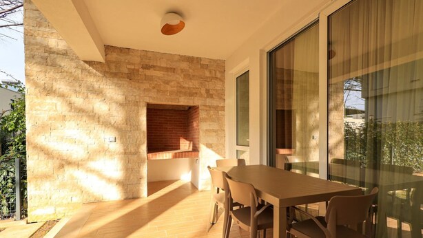 A modern dining area with a brick wall, wooden flooring, and a glass partition. - SanPietro Vacation Apartment 026 (Plazhi San Pietro)