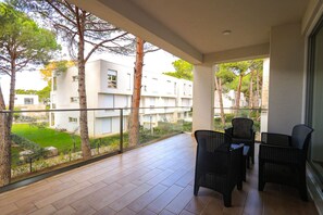 En balkon med udsigt over et boligområde, med siddepladser bestående af fletstole og flisetæppe.