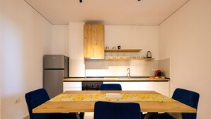A modern kitchen with a built-in refrigerator, stove, and sink. There is a wooden dining table with blue chairs and a yellow floral table runner. - SanPietro Vacation Apartment 032 (Plazhi San Pietro)
