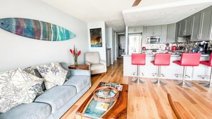 Una sala de estar moderna con un sofá gris, una mesa de centro de madera y una cocina con armarios grises y taburetes rojos.