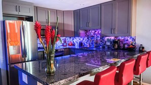 Una cocina moderna con gabinetes grises, un refrigerador de acero inoxidable, una encimera de mármol y taburetes rojos.