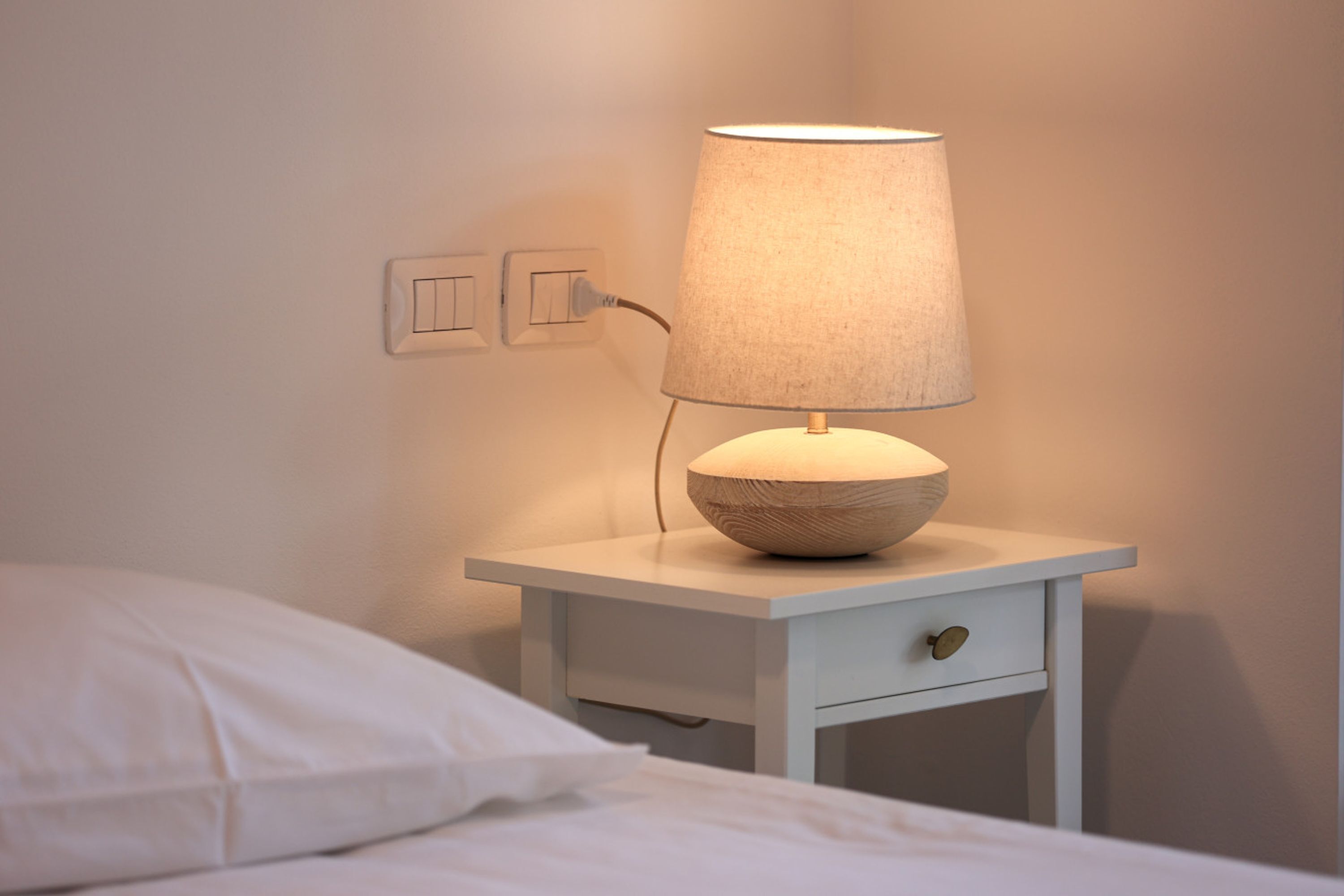 A bedside table with a lamp, a power outlet, and a wall socket.