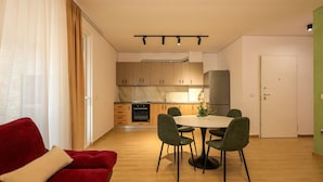 Eine moderne Küche mit Holzschränken, einem Einbauofen und einem Essbereich mit rundem Tisch und grünen Stühlen.