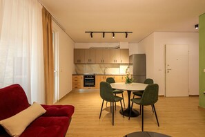 Eine moderne Wohnung mit einem roten Sofa, einem Esstisch mit Stühlen, einer Küche mit Holzausbau und einer grünen Wand.