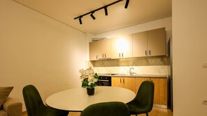 A modern kitchen with wooden cabinets, a white countertop, and a dining area with a round table and two chairs. - SanPietro Vacation Apartment 033 (Durrës)